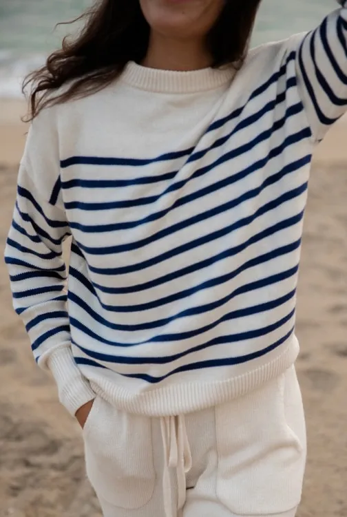 A woman on the beach in a navy-striped Minnow sweater
