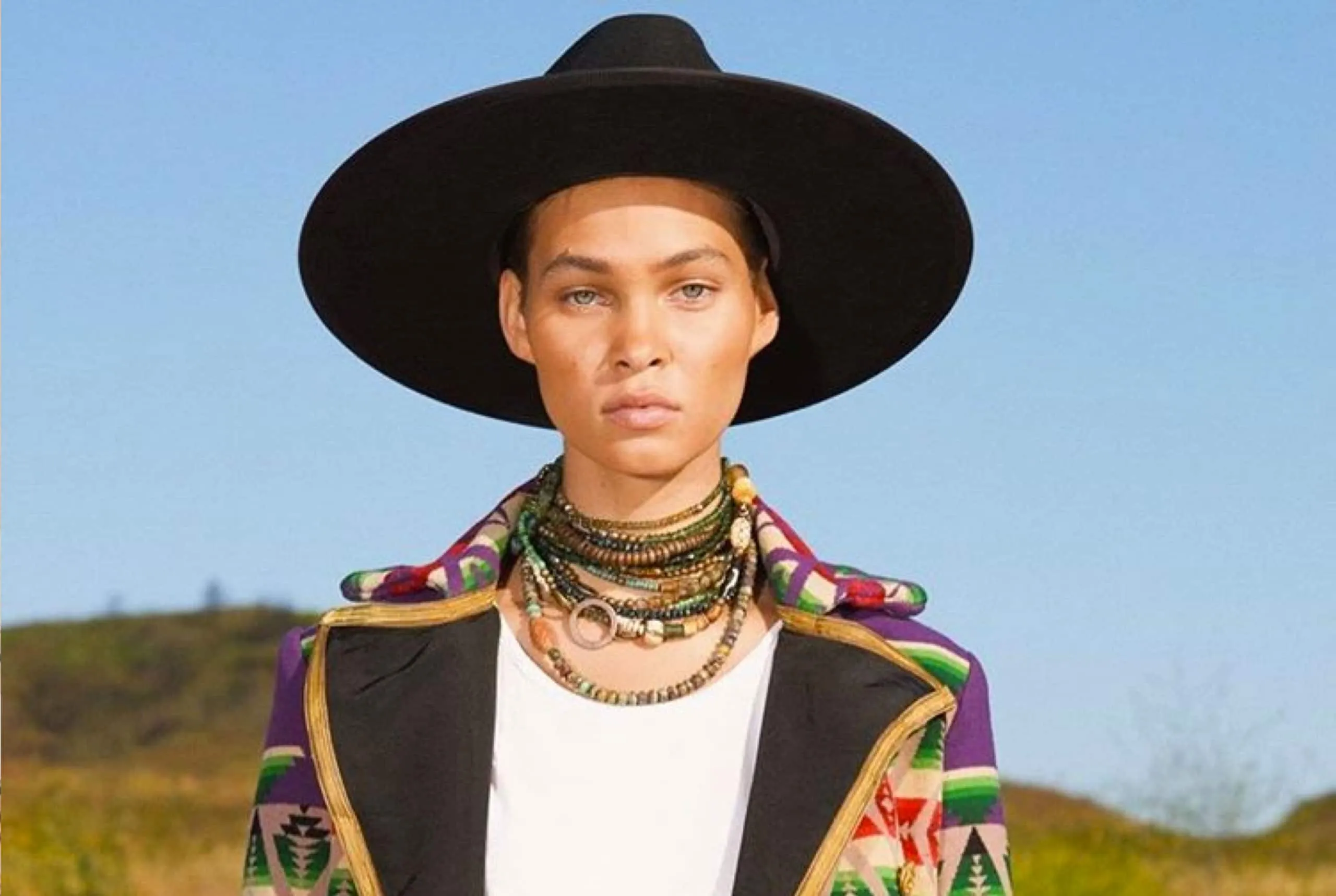 A model on a hillside wearing a wide-brim hat and a patterned Greg Lauren jacket